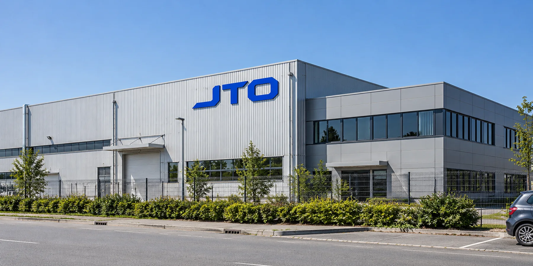 Illustrative light-grey manufacturing building with a glass entrance and freestanding JTO sign.